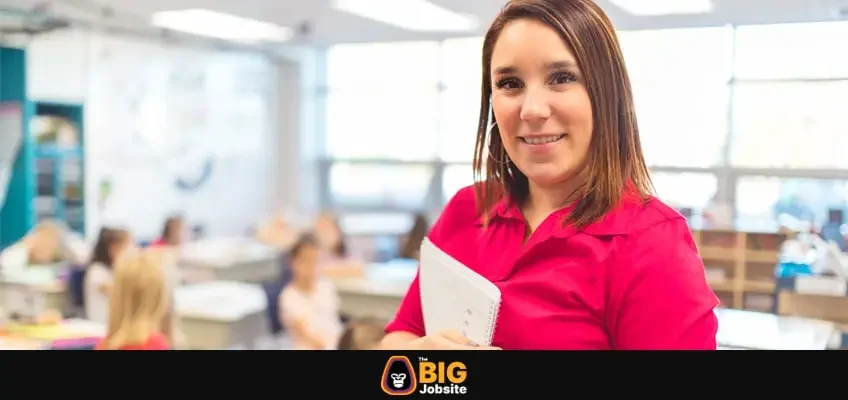 Woman teacher smiling at camera at back of classroom at the elementary school