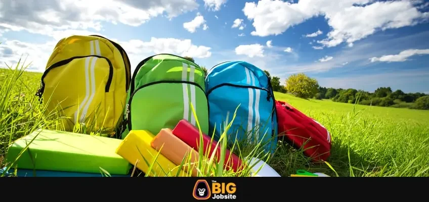 Colourful children schoolbags outdoors on the field. Backpacks with school accessories